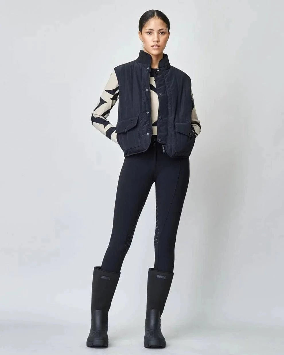 The Black Quilted Riding Vest offers a boxy silhouette with a stand-up collar, front zipper, and placket with easy press studs. The exterior is both wind-proof and water-repellent while Primaloft Padding insulates to provide optimal warmth throughout your ride. Feature two front pockets, two invisible side seam pockets, and an inner pocket. Cut from an Italian fabric, and sewn in Europe.