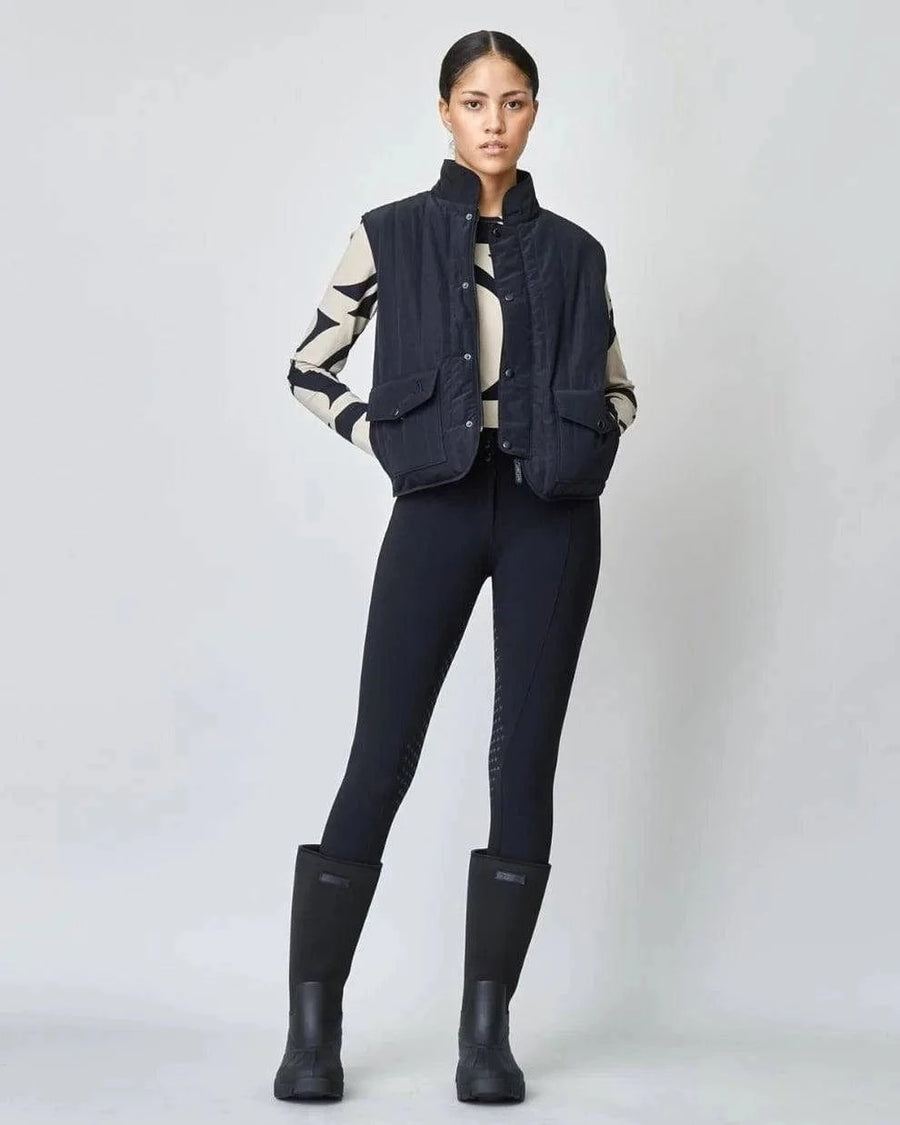 The Black Quilted Riding Vest offers a boxy silhouette with a stand-up collar, front zipper, and placket with easy press studs. The exterior is both wind-proof and water-repellent while Primaloft Padding insulates to provide optimal warmth throughout your ride. Feature two front pockets, two invisible side seam pockets, and an inner pocket. Cut from an Italian fabric, and sewn in Europe. 